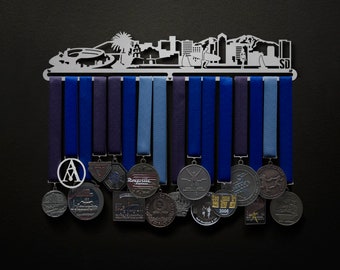 May include: A silver metal medal rack shaped like a city skyline with 15 medals hanging from it. The medals are silver, gold, and bronze and feature various designs.