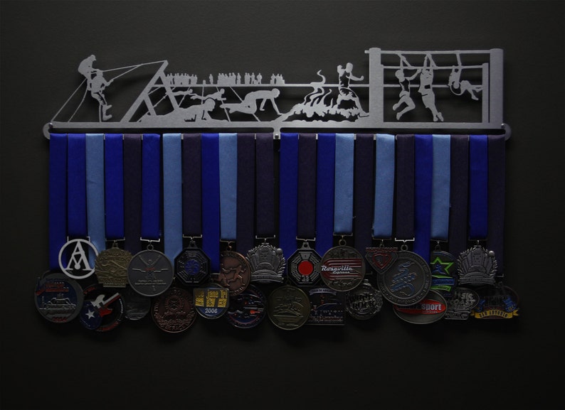 May include: A metal medal display rack with a silhouette of athletes participating in an obstacle course. The rack has 17 blue and light blue medal hangers. The rack is decorated with 17 medals of various shapes, sizes, and designs. The medals are silver, gold, and bronze in color.