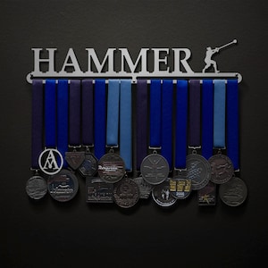 May include: A silver metal medal rack with the word "HAMMER" in large letters. The rack has a silhouette of a person throwing a hammer. There are 12 blue and purple ribbons hanging from the rack with various medals attached.