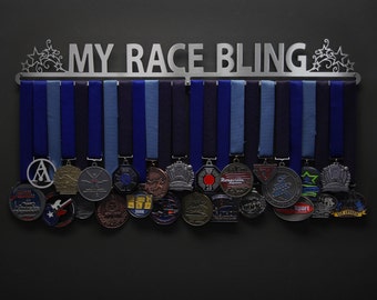 May include: A silver metal medal display rack with the text "MY RACE BLING" and decorative star accents. The rack holds numerous race medals suspended from blue ribbons. The medals vary in design and color, showcasing achievements.