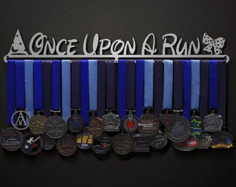 May include: A silver metal medal display rack with the words "Once Upon A Run" and a bow. The rack has blue and black ribbons hanging from it with medals attached.