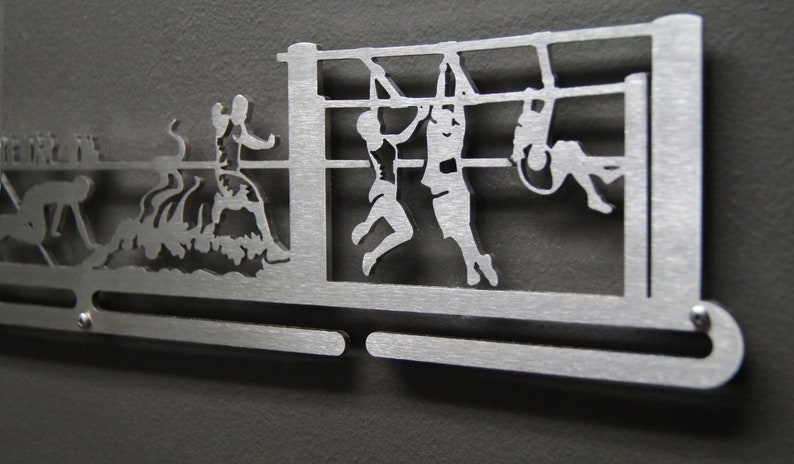 Puede incluir: Un colgador de medallas de metal plateado con un dise&ntilde;o de ni&ntilde;os jugando deportes. El colgador tiene dos barras para colgar medallas. El dise&ntilde;o incluye un ni&ntilde;o nadando, un ni&ntilde;o jugando al baloncesto y dos ni&ntilde;os en una barra de mono.