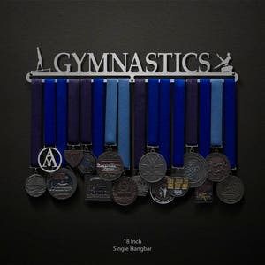May include: An 18-inch single hangbar medal display with the word "GYMNASTICS" in silver metal lettering. The hangbar is decorated with silver metal gymnast silhouettes. The hangbar is holding a collection of blue, silver, and black medals.