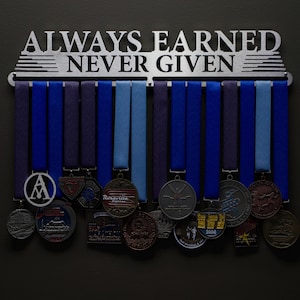 May include: A silver medal display rack with the words "Always Earned Never Given" on it. The rack is holding a collection of blue, purple, and light blue ribbons with various medals attached.