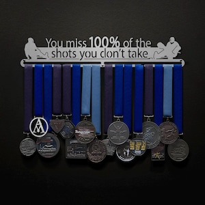 May include: A silver medal display rack with the quote "You miss 100% of the shots you don't take."  The rack has a silhouette of a person in a racing sled.  The rack is holding a variety of medals with blue and purple ribbons.