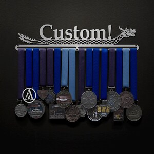 May include: A silver metal medal display rack shaped like a dragon with the word "Custom!" on it. The rack has 15 blue and purple ribbons hanging from it with various medals attached.