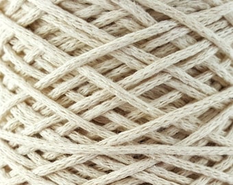 May include: A close-up of a spool of natural-colored cotton yarn. The yarn is tightly wound and has a rough texture.