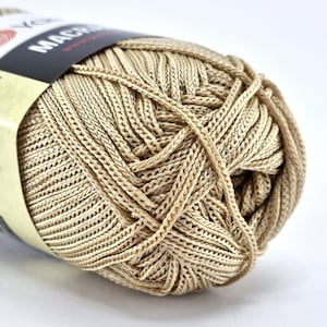 Könnte beinhalten: Eine Rolle beigefarbener Wolle mit einem Etikett, auf dem "MACRAME" in schwarzer Schrift steht.