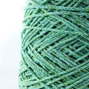 May include: A close-up of a spool of teal green yarn with gold glitter thread woven throughout.