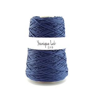 May include: A spool of navy blue yarn with the text "Younique Lab ER7" on a white label. The yarn is tightly wound, showing a textured surface. The background is plain white.
