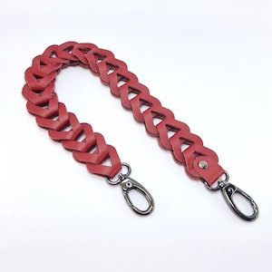 Könnte beinhalten: Roter geflochtener Lederriemen mit zwei silbernen Metallschließen. Der Riemen ist in einem Herzmuster gewebt.