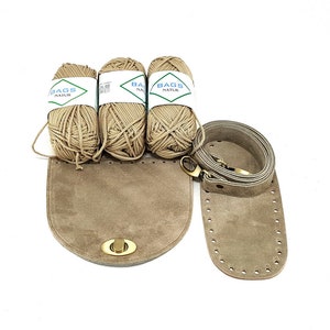 May include: Three balls of beige yarn labeled "Bags Natur" and a suede leather kit for making a bag. The kit includes a bag bottom, a strap, and a brass clasp.
