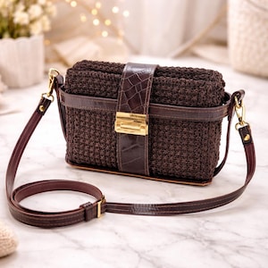 May include: A brown crochet crossbody bag with a leather strap and a gold-colored clasp. The bag features a rectangular shape with a textured crochet design and a crocodile-embossed leather flap. The adjustable strap is made of brown leather.
