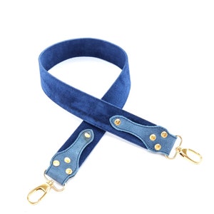 Peut inclure: Une sangle de caméra en daim bleu avec des ferrures en métal doré et deux clips pivotants.