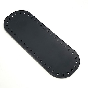 Peut inclure: Sangle en cuir noir avec des trous espacés uniformément sur les bords. La sangle est rectangulaire avec des extrémités arrondies.