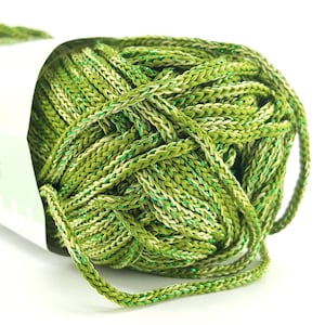 May include: Close-up of a ball of green yarn with a braided texture. The yarn has a mix of light and dark green shades with a subtle metallic sheen. The yarn is partially visible, emerging from a white label.