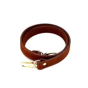 May include: A brown suede leather strap with gold hardware. The strap has a single gold snap and two gold hooks.