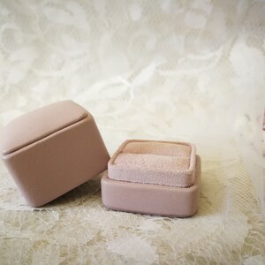 May include: Two pink ring boxes with a velvet interior. The boxes are on a white lace background.