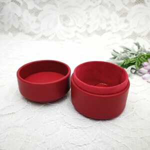 May include: A red ring box with a velvet lining. The box is open and the lid is sitting next to it.