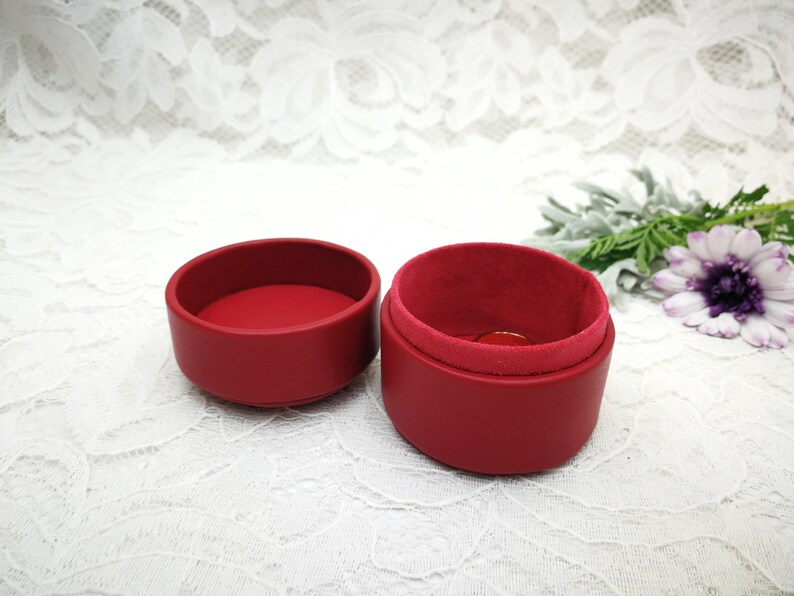 May include: A red ring box with a velvet lining. The box is open and the lid is sitting next to it.