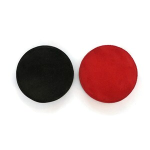 May include: Two round coasters. One is black, the other is red. Both are made of a soft, suede-like material. The coasters are circular and appear to be about 4 inches in diameter.