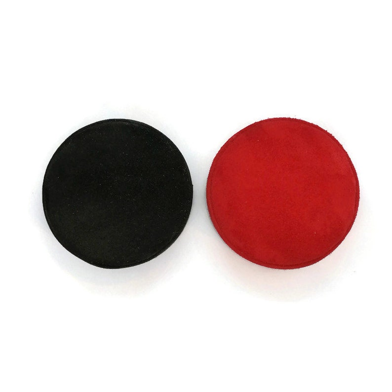 May include: Two round coasters. One is black, the other is red. Both are made of a soft, suede-like material. The coasters are circular and appear to be about 4 inches in diameter.