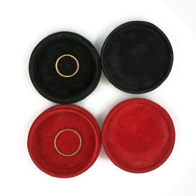 May include: Four small, round jewelry trays in black and red. Two black trays and two red trays are visible. Each tray has a gold ring inside. The trays are made of a soft, velvety material.