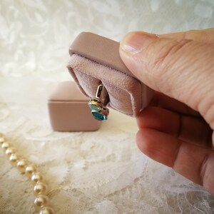 May include: A pair of blue gemstone earrings in a pink velvet jewelry box.