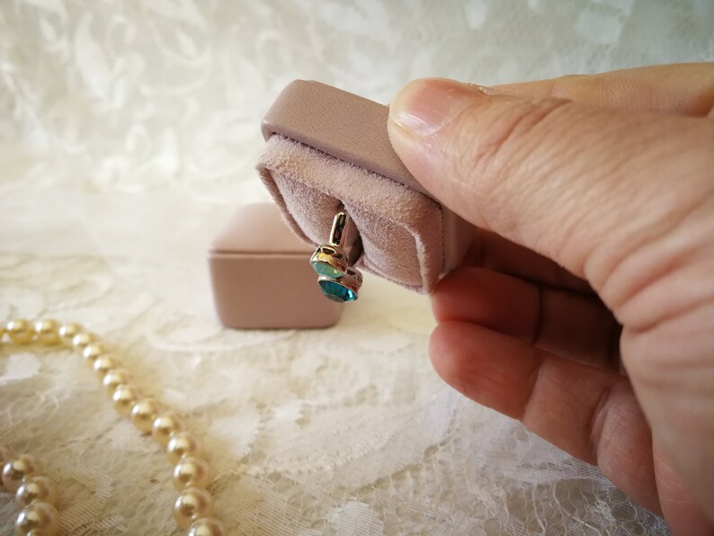 May include: A pair of blue gemstone earrings in a pink velvet jewelry box.