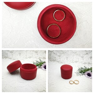 May include: Two red ring boxes with velvet interiors. One box is open and contains two gold rings. The other box is closed.