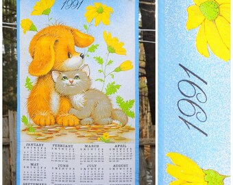 Puede incluir: Una toalla de cocina azul y amarilla con un calendario de 1991 que presenta un cachorro y un gatito. El calendario incluye los meses de enero a diciembre.