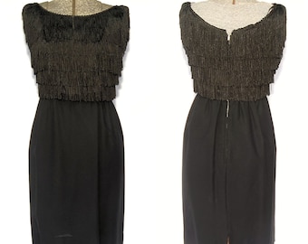 May include: A black sleeveless dress with a fringe trim around the neckline and waist. The dress has a fitted bodice and a straight skirt.