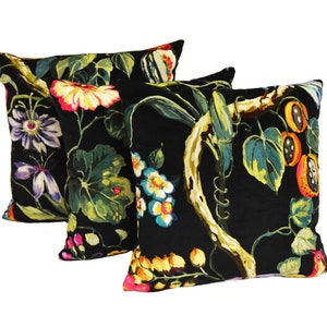May include: Three black velvet throw pillows with a floral and fruit print. The print features bright colors like red, yellow, orange, pink, and blue.