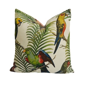 Puede incluir: Una almohada blanca con un estampado tropical que presenta hojas de palmera verdes y loros coloridos. Los loros son verdes, rojos, amarillos y azules.
