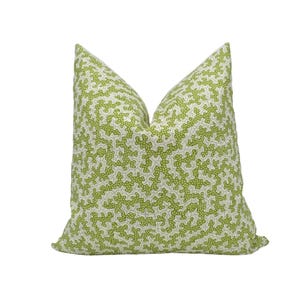 Pode incluir: Uma almofada quadrada com um padrão repetitivo de formas orgânicas verde-limão que lembram coral sobre um fundo branco. O tecido tem uma aparência texturizada com pequenos pontos preenchendo as formas verdes, criando um design denso e ramificado.