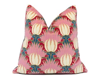 May include: A pink and red pillow with a floral pattern featuring white tulips and gold accents. The pillow has a navy blue border.