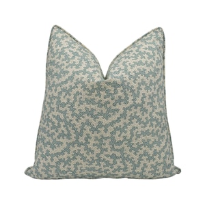 May include: A square cushion featuring a light blue and beige pattern. The design is a repeating pattern of interconnected shapes, giving a textured look. This cushion is a soft, neutral accent for any room.