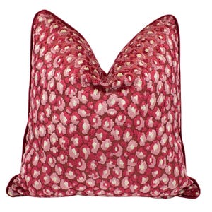 May include: A decorative throw pillow with a vibrant red and white leopard print pattern. The pillow has a dark red border and is designed for home decor. The pillow is square-shaped and has a soft, textured appearance.