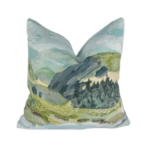May include: A decorative cushion featuring a landscape design with a mountain range, trees, and a sky with clouds. The cushion is made from a soft, light blue fabric.