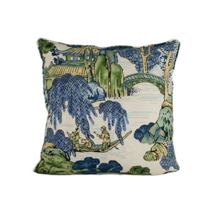 May include: A decorative throw pillow with a blue and green landscape design featuring a bridge, trees, and figures in a boat. The background is a light cream color.