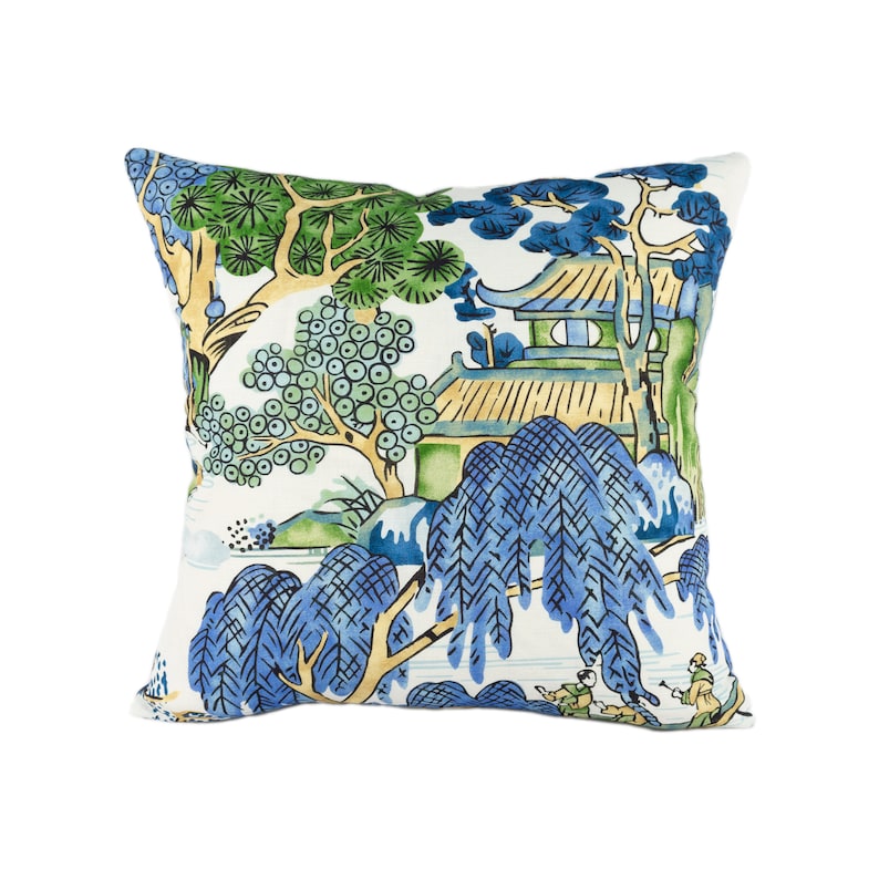 May include: A white throw pillow with a blue and green Asian-inspired design. The pillow features a pagoda, trees, and a river with figures in the foreground.