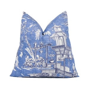 Puede incluir: Almohada azul y blanca con un diseño tradicional de jardín chino. La almohada presenta una pagoda, árboles y figuras en un patrón azul y blanco.