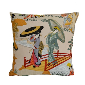 May include: A decorative pillow with a beige background featuring a Japanese-inspired design. The pillow features two women in traditional clothing holding umbrellas, walking across a red bridge over a stream. The design is filled with vibrant colors and intricate details.
