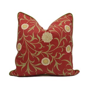 May include: Red pillow with a green border and a floral pattern featuring white flowers and green leaves.