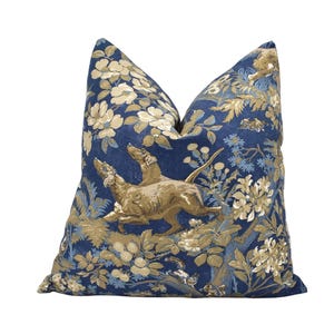 May include: A square cushion with a blue background and a floral and dog design. The cushion features a detailed pattern of beige flowers and foliage, with two dogs in the center. The cushion has a soft, inviting appearance and is suitable for a sofa or bed.