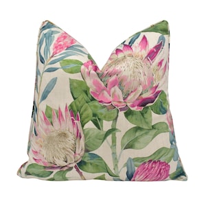 May include: A cream-colored pillow with a floral print featuring pink and white proteas and green leaves.