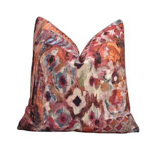 May include: A decorative cushion with a colourful abstract pattern in shades of red, orange, blue, and white. The cushion has a soft, textured fabric and a square shape.