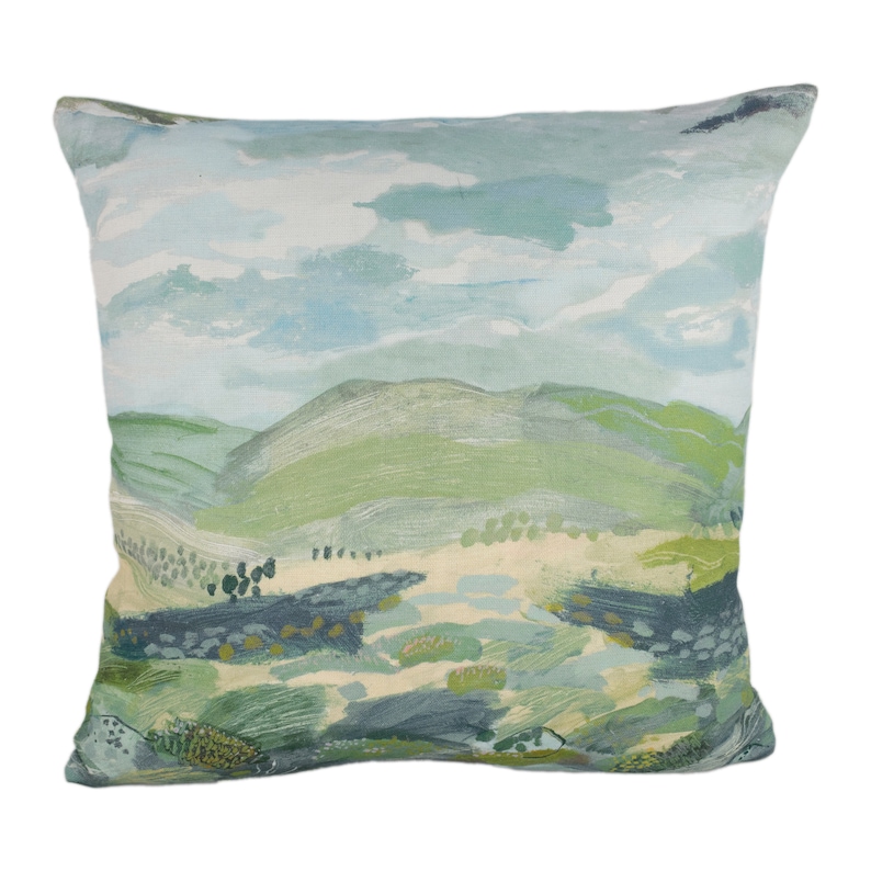 May include: A decorative cushion with a watercolour-style landscape design. The cushion features a blue sky with white clouds, green hills, and a light brown path.