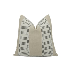 May include: A beige linen pillow with a black and white striped pattern on the front. The stripes are arranged in a geometric design.