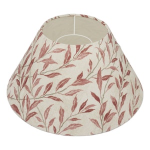 May include: A beige lampshade with a red leaf pattern. The lampshade is cone-shaped and has a white lining.